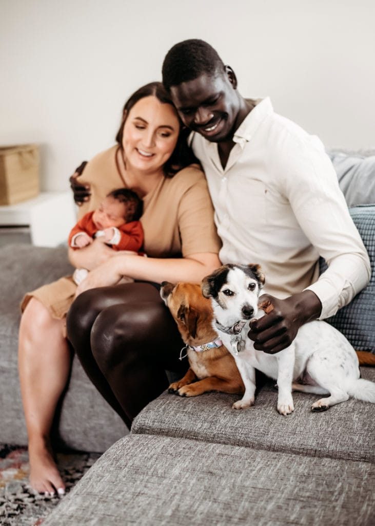 Newborn Photographer New mother and father sit with their baby and puppy on the couch