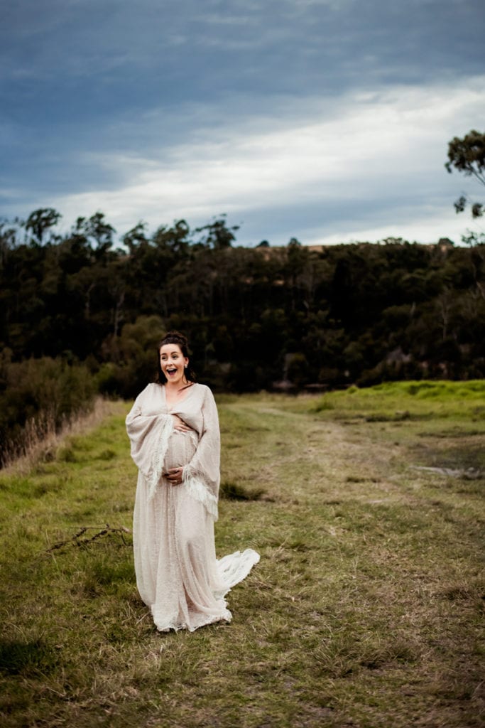 Maternity Photographer, An excited and expectant mother walks down a grassy hillside smiling